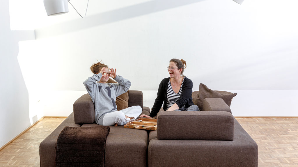 Ein Kind albert auf dem Sofa herum, eine erwachsene Frau lacht. Das Sofa ist zu einer quadratischen Fläche gestellt worden