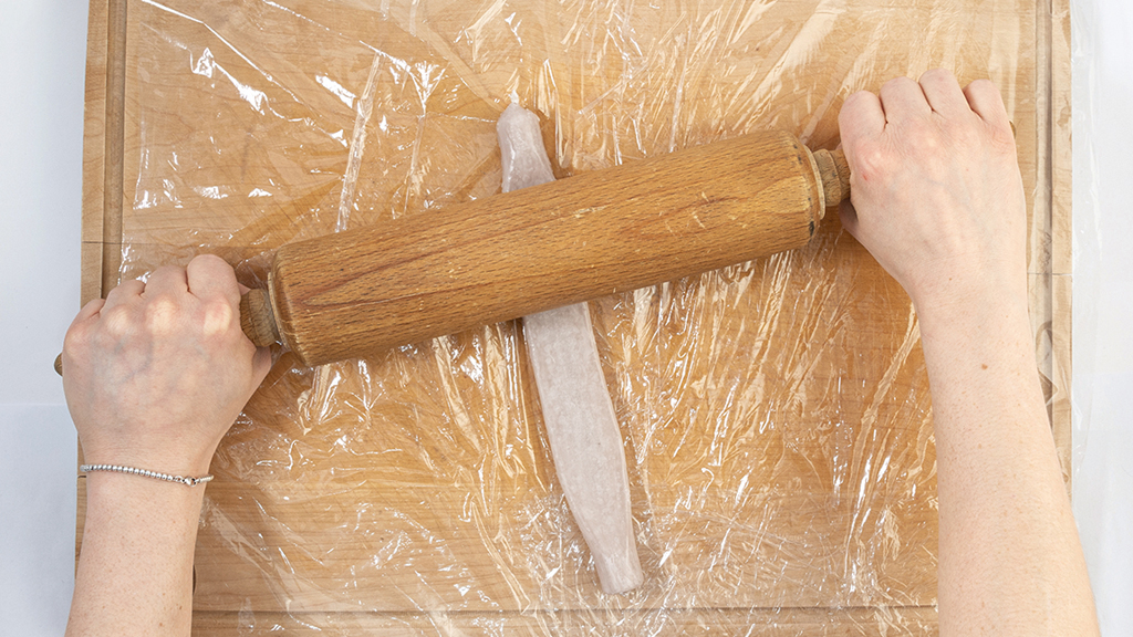 Eine weiche Stabkerze wird mit einem Nudelholz auf einem Schneidebrett platt gerollt. An beiden Enden bleiben sie circa 1,5 Zentimeter rund