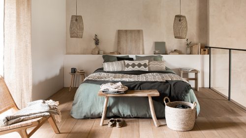 Bett mit grünem Bettbezug und braunen Kissen vor einer braunen Wand