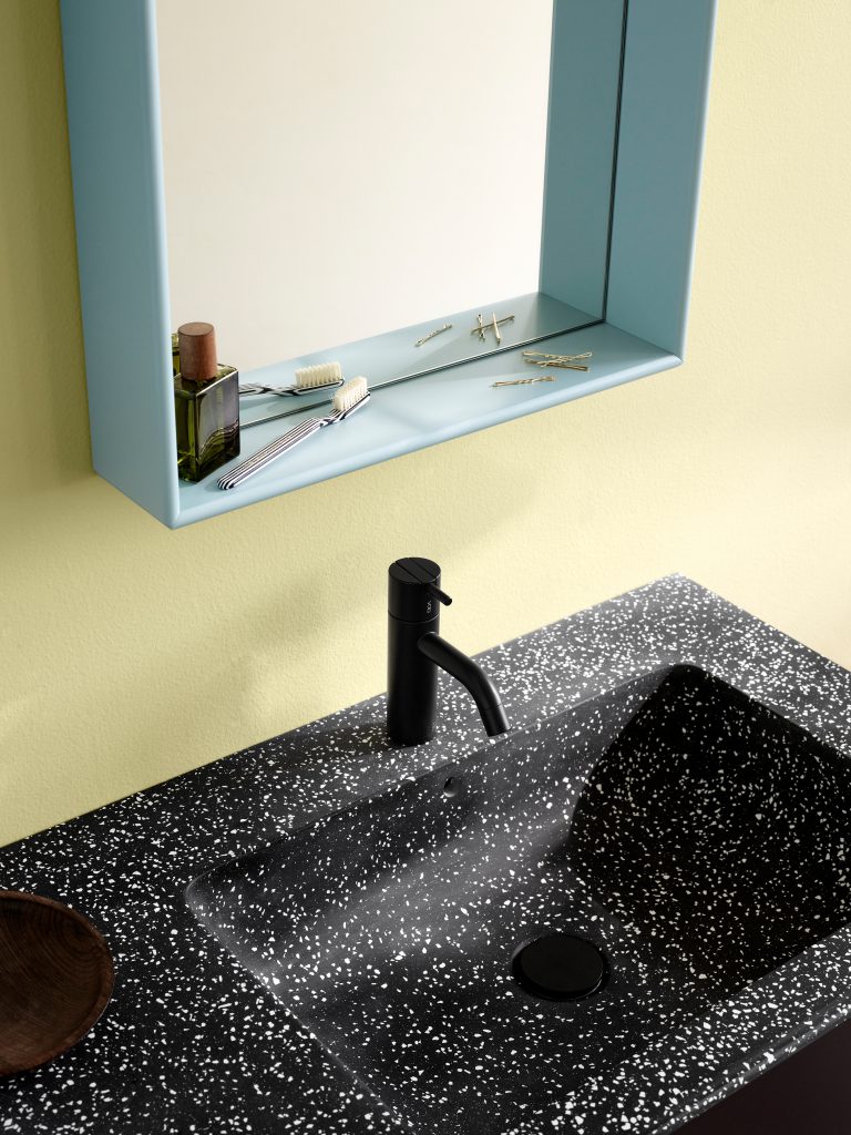 Blick auf einen schwarz/weiß gesprenckelten Waschtisch aus Naturstein. Darüber hängt ein hellblauer Spiegel mit großem Regalrahmen. 