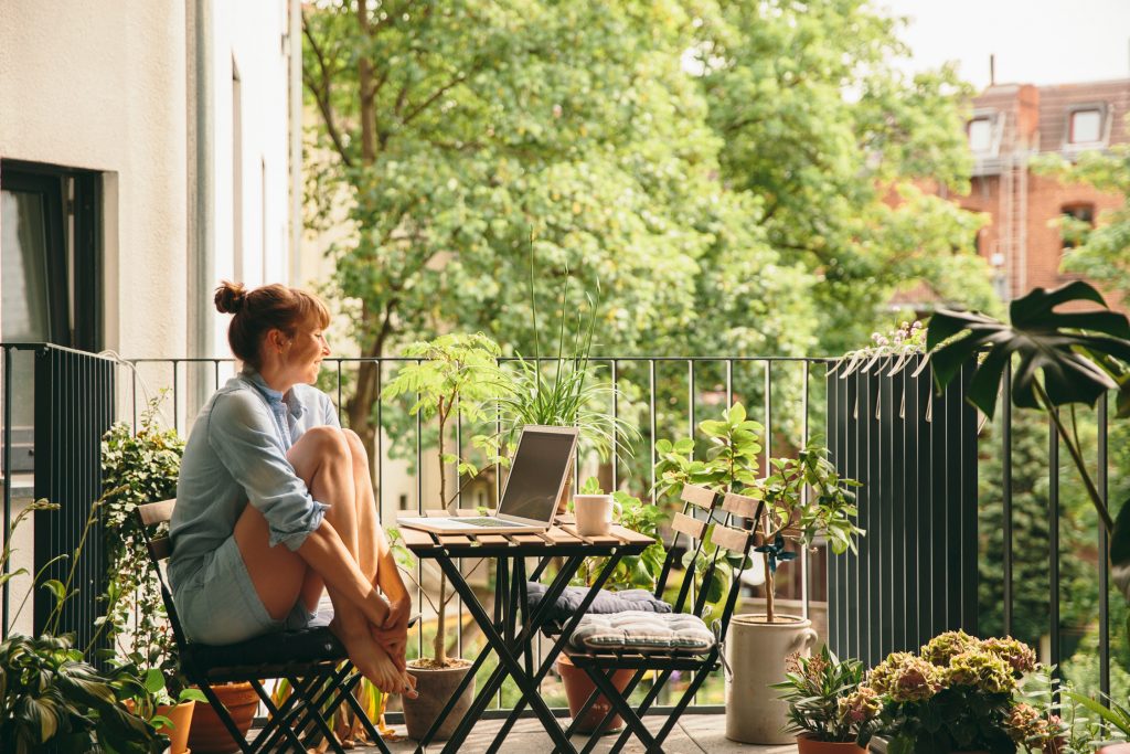 Eine Frau sitzt mit ihrem Laptop auf dem Balkon im Grünen
